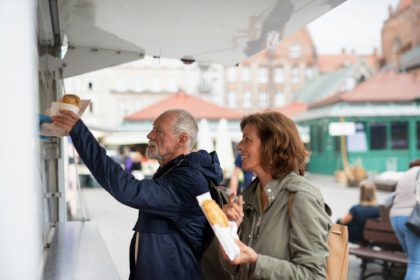 Happy senior couple tourists buying snack outdoors in street