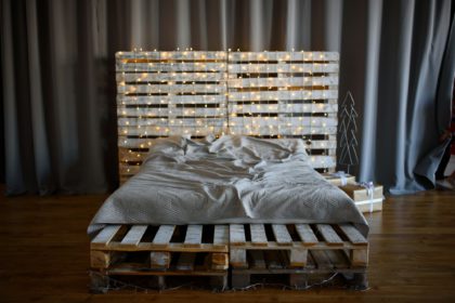 Modern interior. The bed is made from pallets, decorated with garlands and gifts.