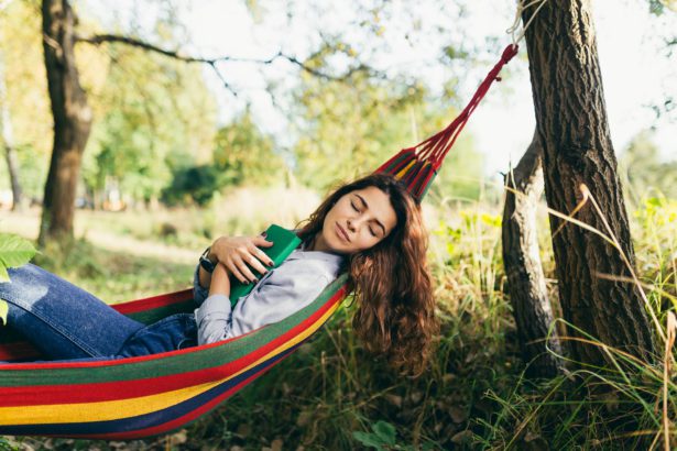 Young beautiful woman resting in nature, lying in a hammock, reading a book, vacation